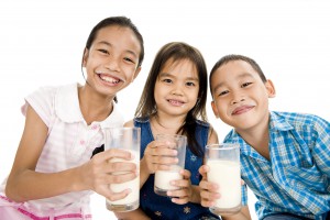 three asian kids with glasses of milk, isolated on white background